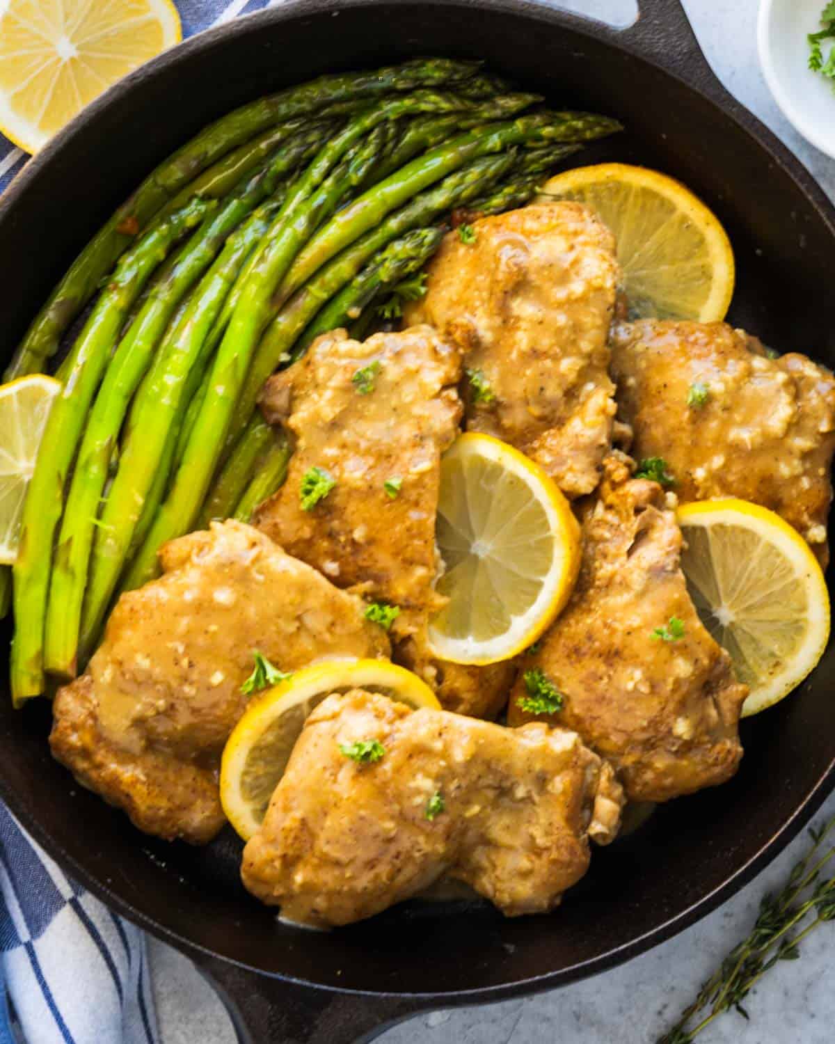 a black pan with chicken, slices of lemons and asparagus