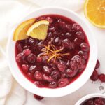 bowl of cranberry sauce surrounded by oranges and cranberries.