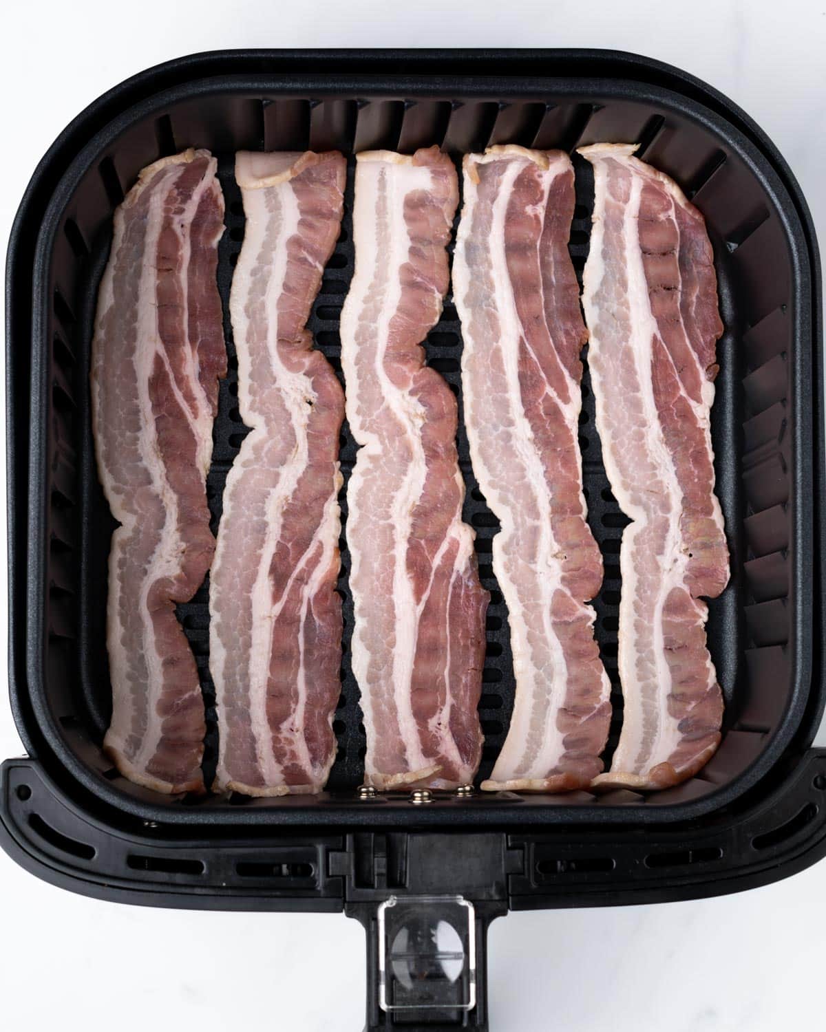 Bacon in an air fryer basket.