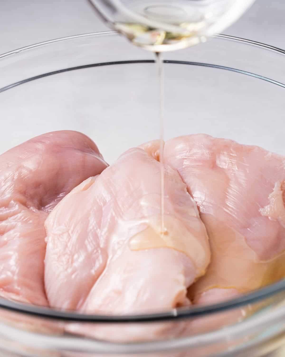 Drizzling olive oil on chicken breast.