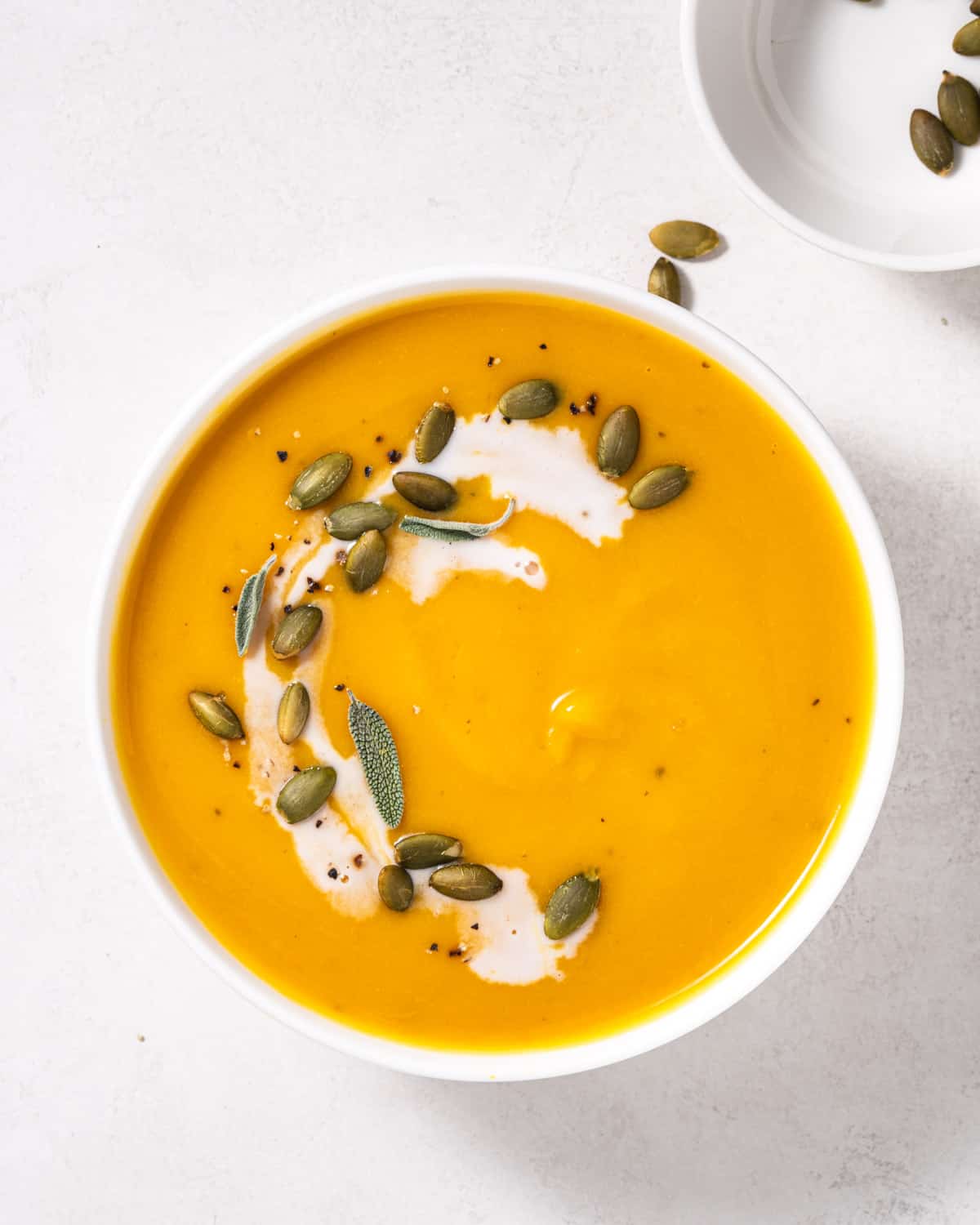 Bowl of instant pot butternut squash soup with coconut milk drizzle, pepitas and sage.