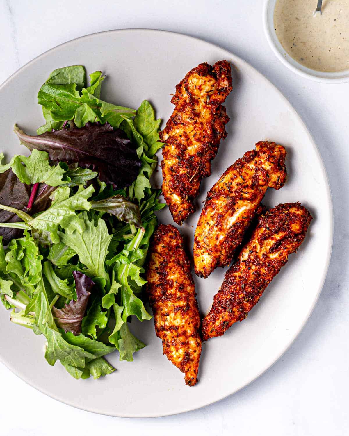 air fryer chicken tenders on a plate with a side of salad and dipping sauce.