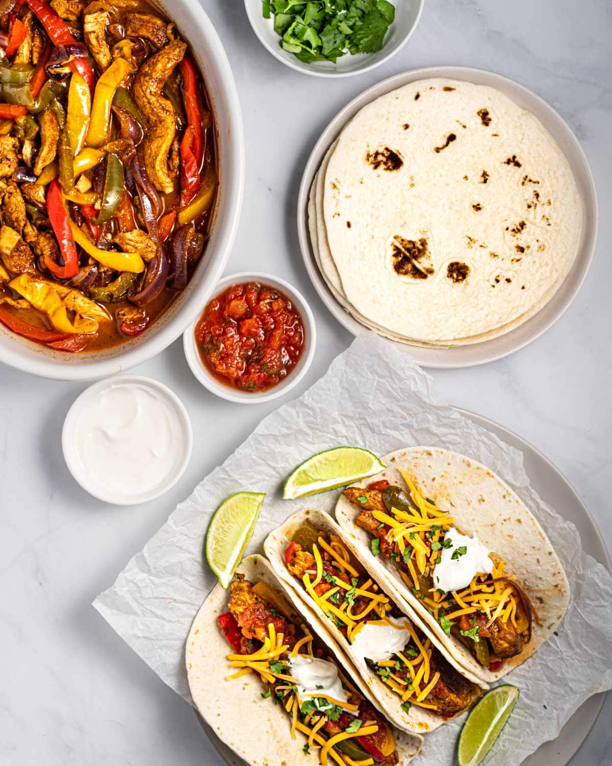 serving bowl of instant pot chicken fajitas, plate with 3 tacos and bowls of toppings.