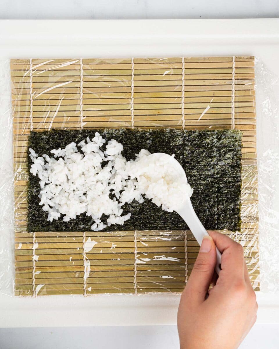 Spatula spreading sushi rice on nori sheet.