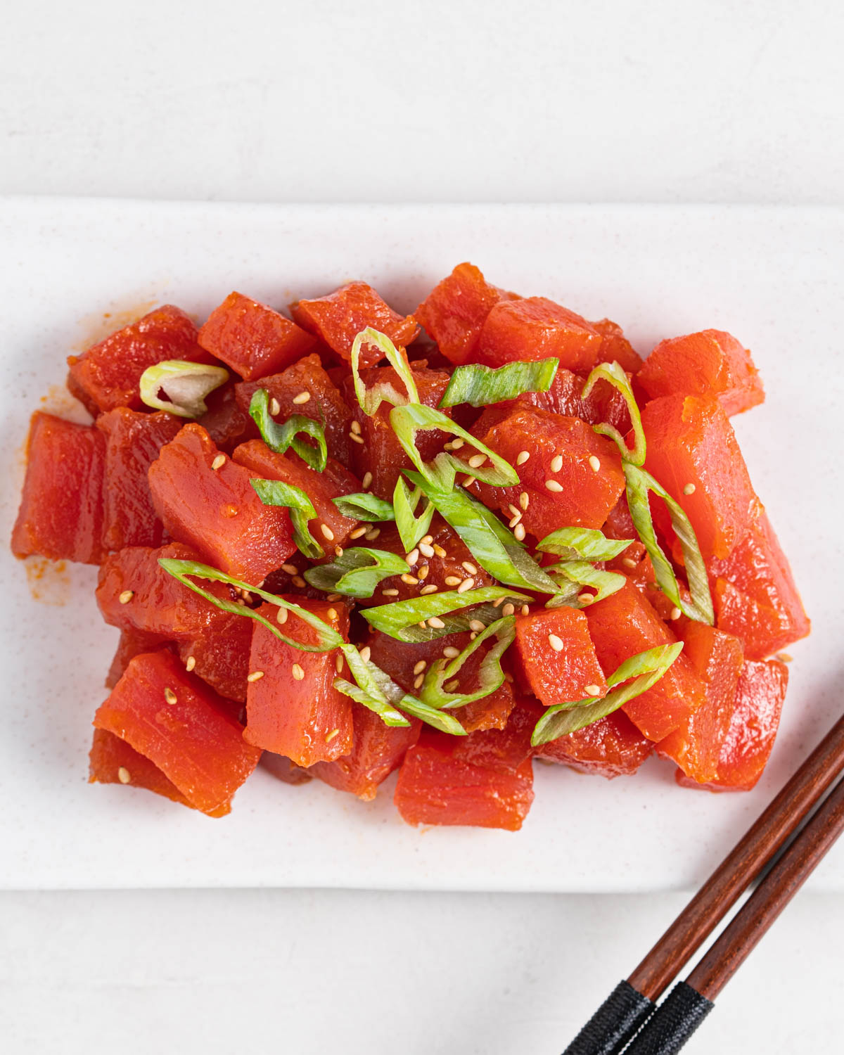 spicy tuna topped with green onions and sesame seeds on a plate with chopsticks on the side.