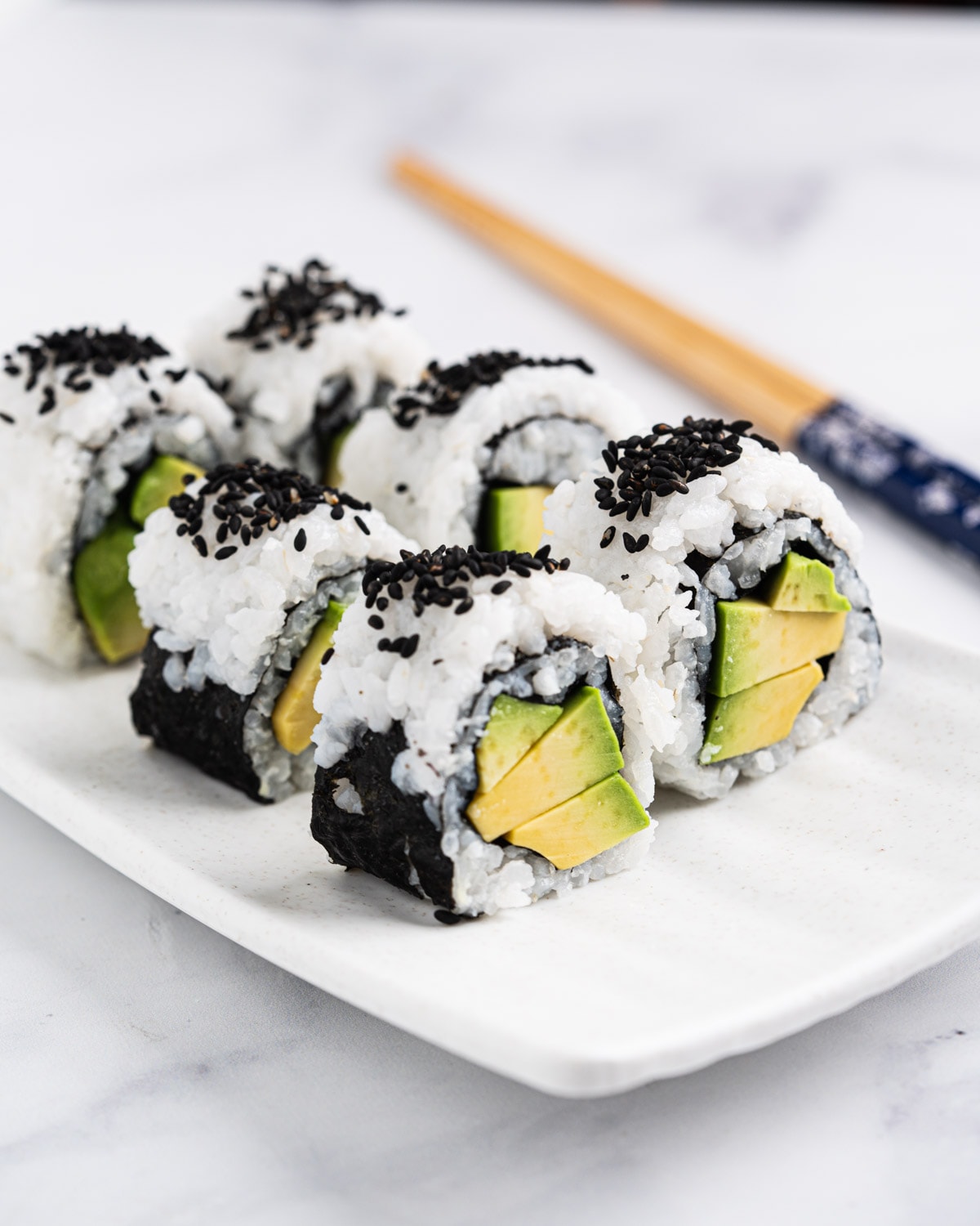 side view of avocado rolls standing up on a plate with chopsticks in the background.