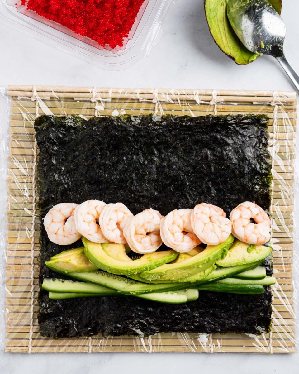 Nori with rice, cucumber, avocado and shrimp on a bamboo sushi rolling mat.