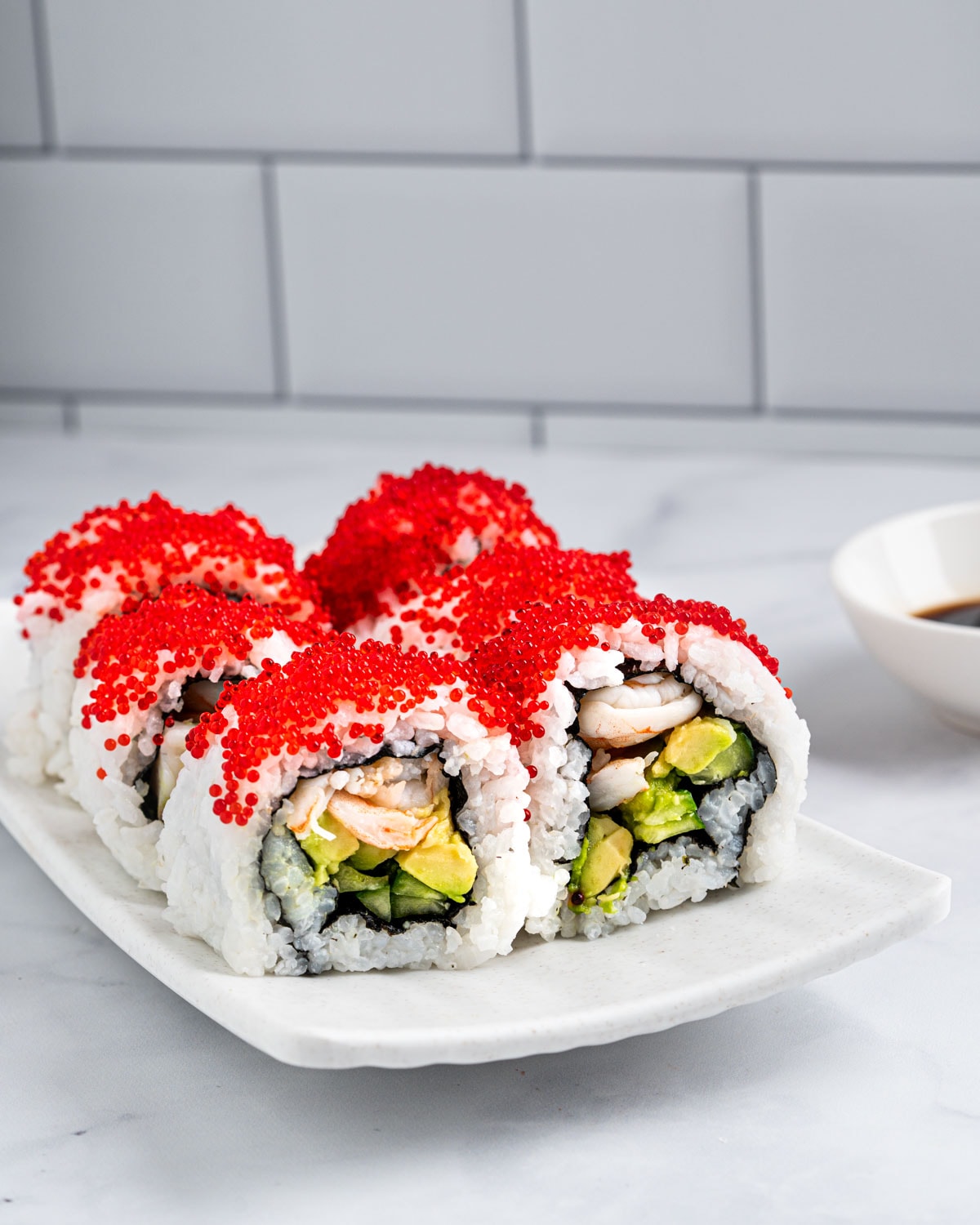 6 Boston Rolls topped with tobiko standing up on a white plate showing the filling which contains poached shrimp, avocado and cucumber.