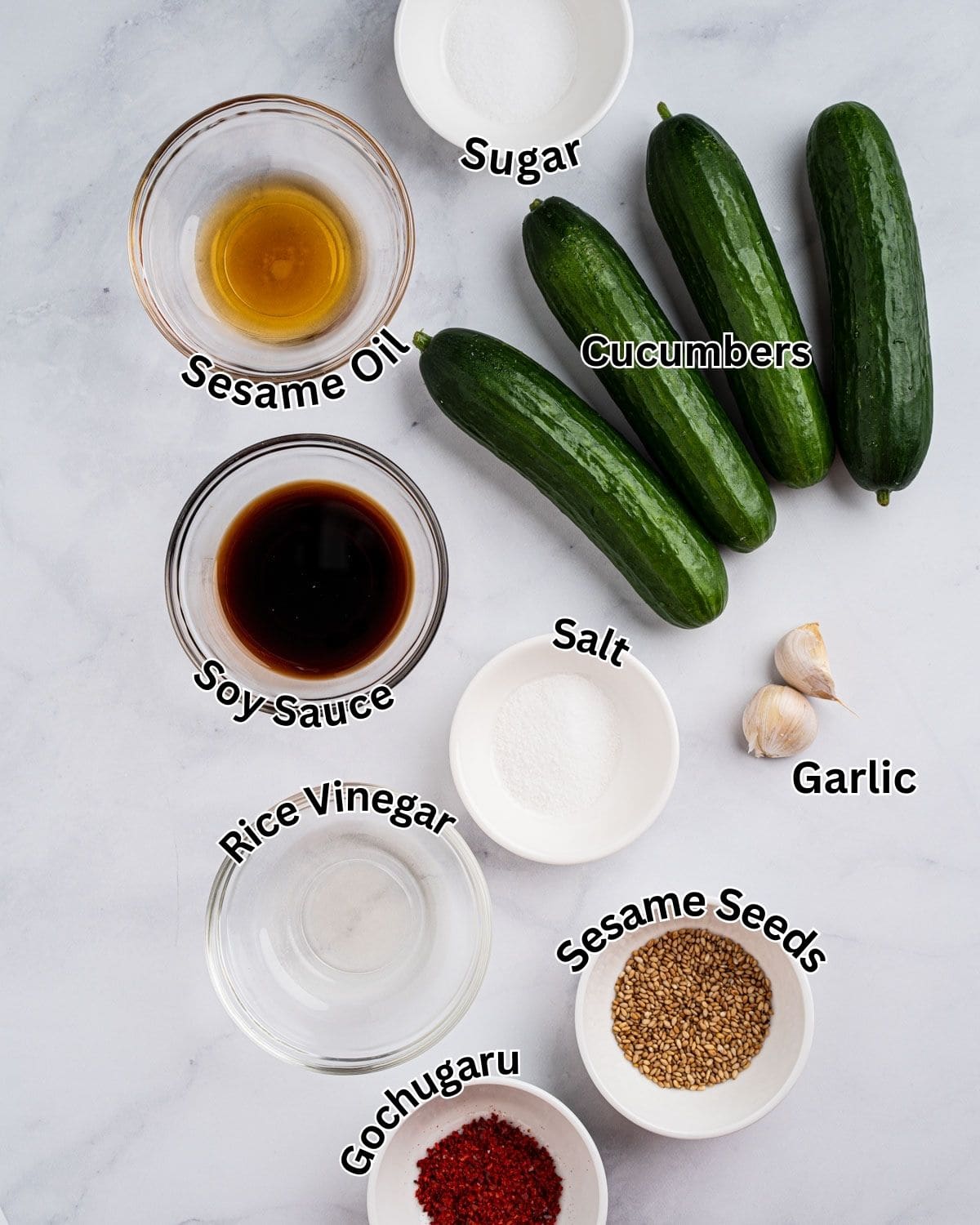Ingredients needed for a spiral Asian cucumber salad: cucumbers, salt, sugar, sesame oil, soy sauce, rice vinegar, gochugaru, garlic, and sesame seeds.