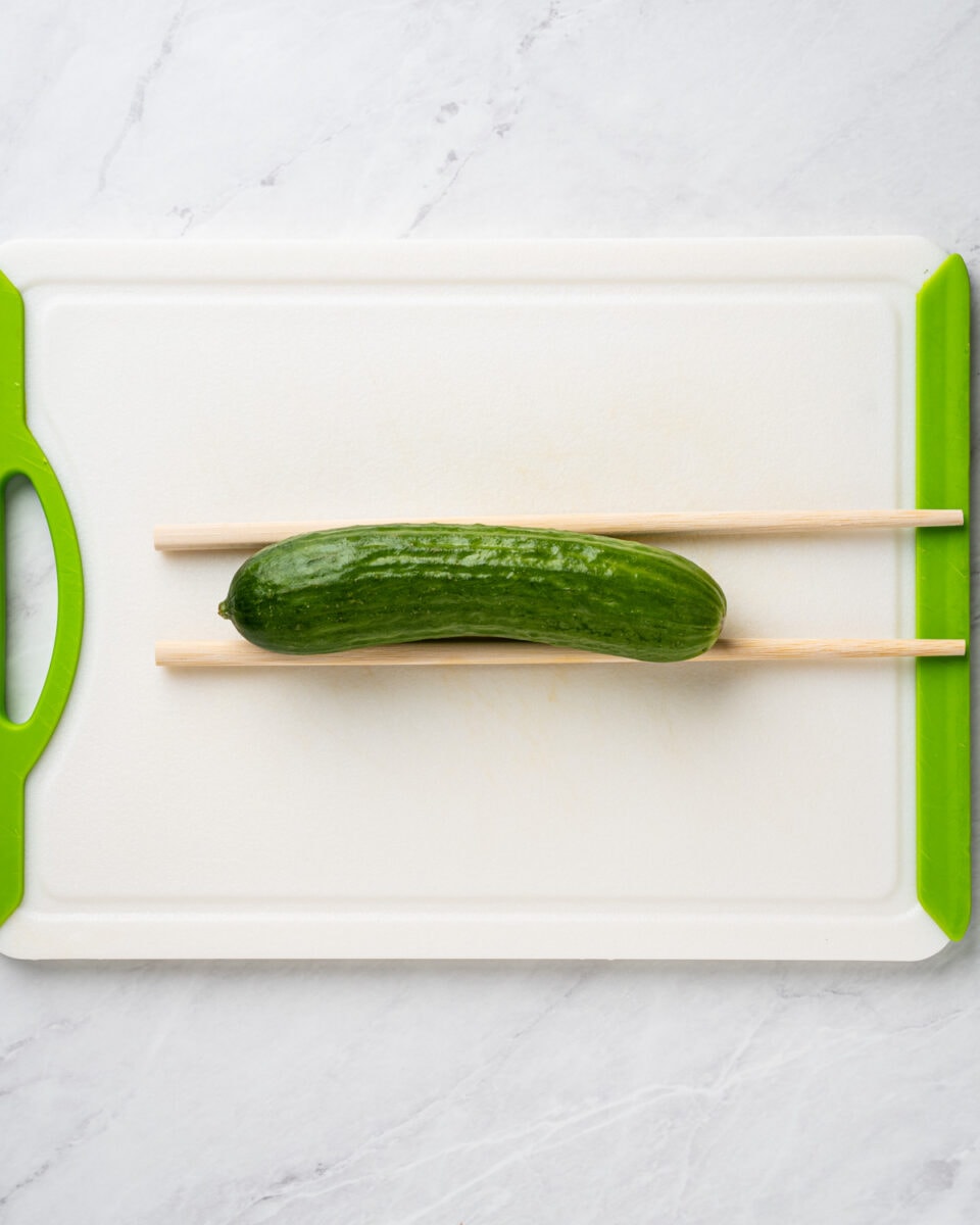 cucumber on a cutting board between two chopsticks.