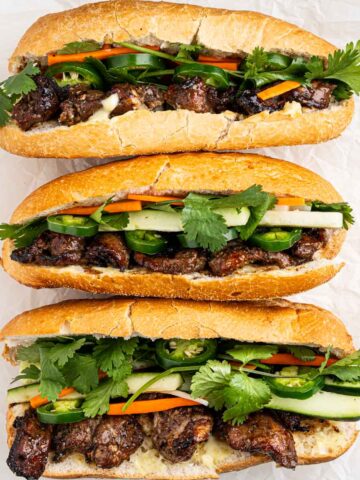 top down of three banh mi thit nuong with grilled pork, pickled vegetables, cucumbers, cilantro and sliced jalapeños.