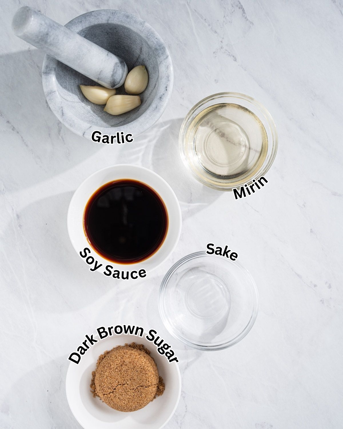 Ingredients needed for eel sauce with labels on a marble countertop. Soy sauce, dark brown sugar, mirin, sake, and garlic.