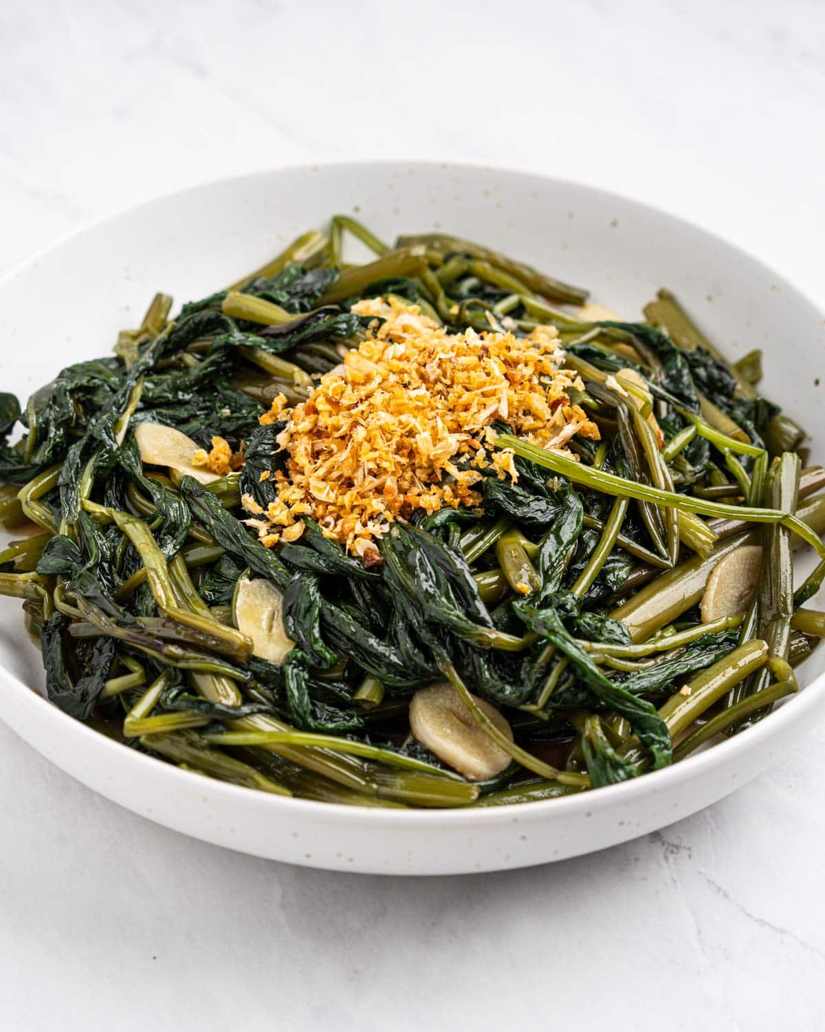 Plate of water spinach stir fried with garlic slices and topped with fried garlic.