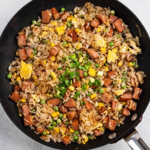 Spam fried rice in a pan garnished with sliced scallions.