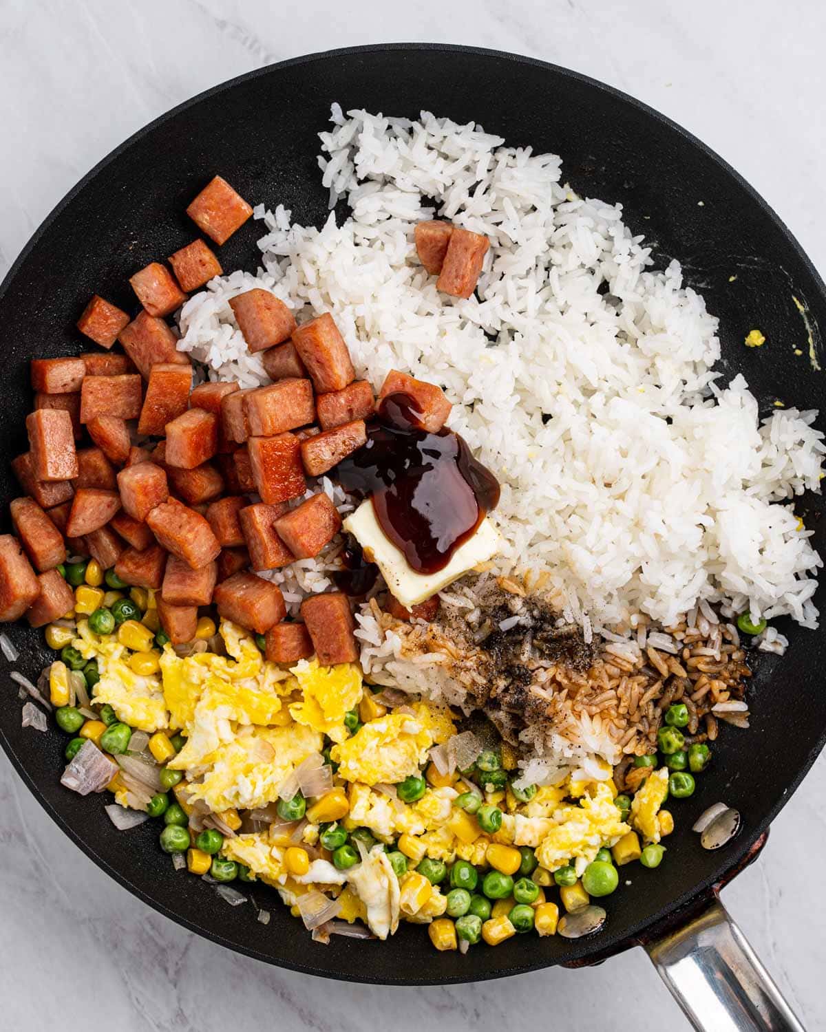 Pan with sections of rice, vegetables, scrambled eggs, spam, seasoning, and butter.