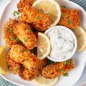 Air Fryer fish sticks on a plate with lemon wedges and white dipping sauce.