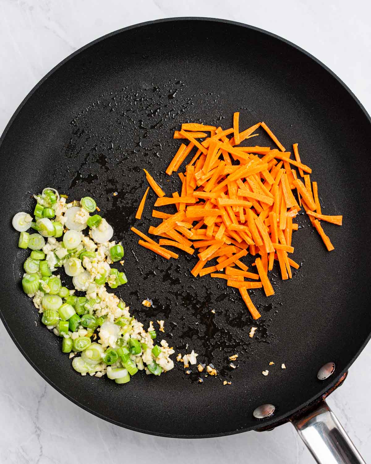 Pan with garlic and green onions on one side and shredded carrots on the other.