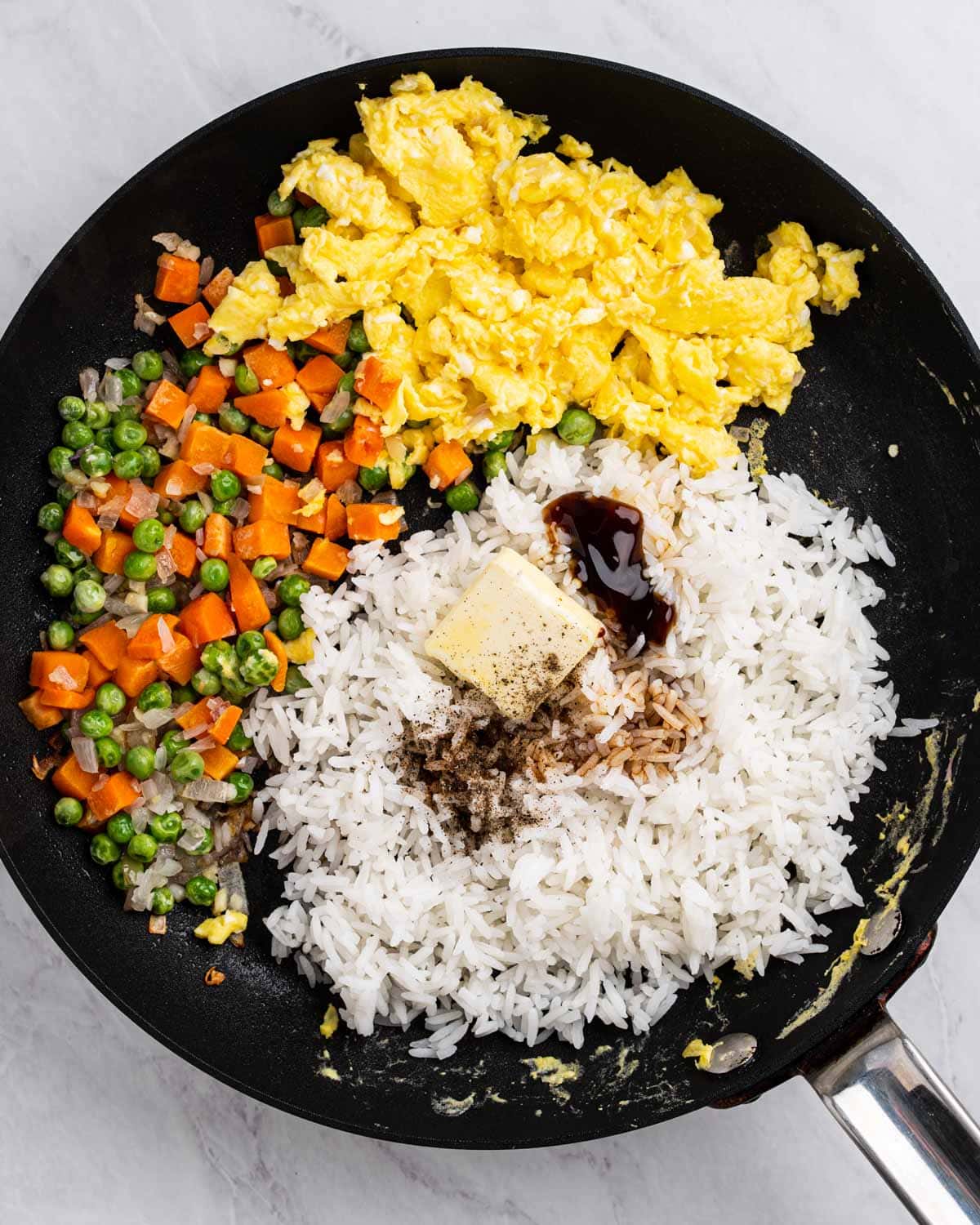 Pan with sautéed vegetables, scrambled eggs, rice, and seasoning.