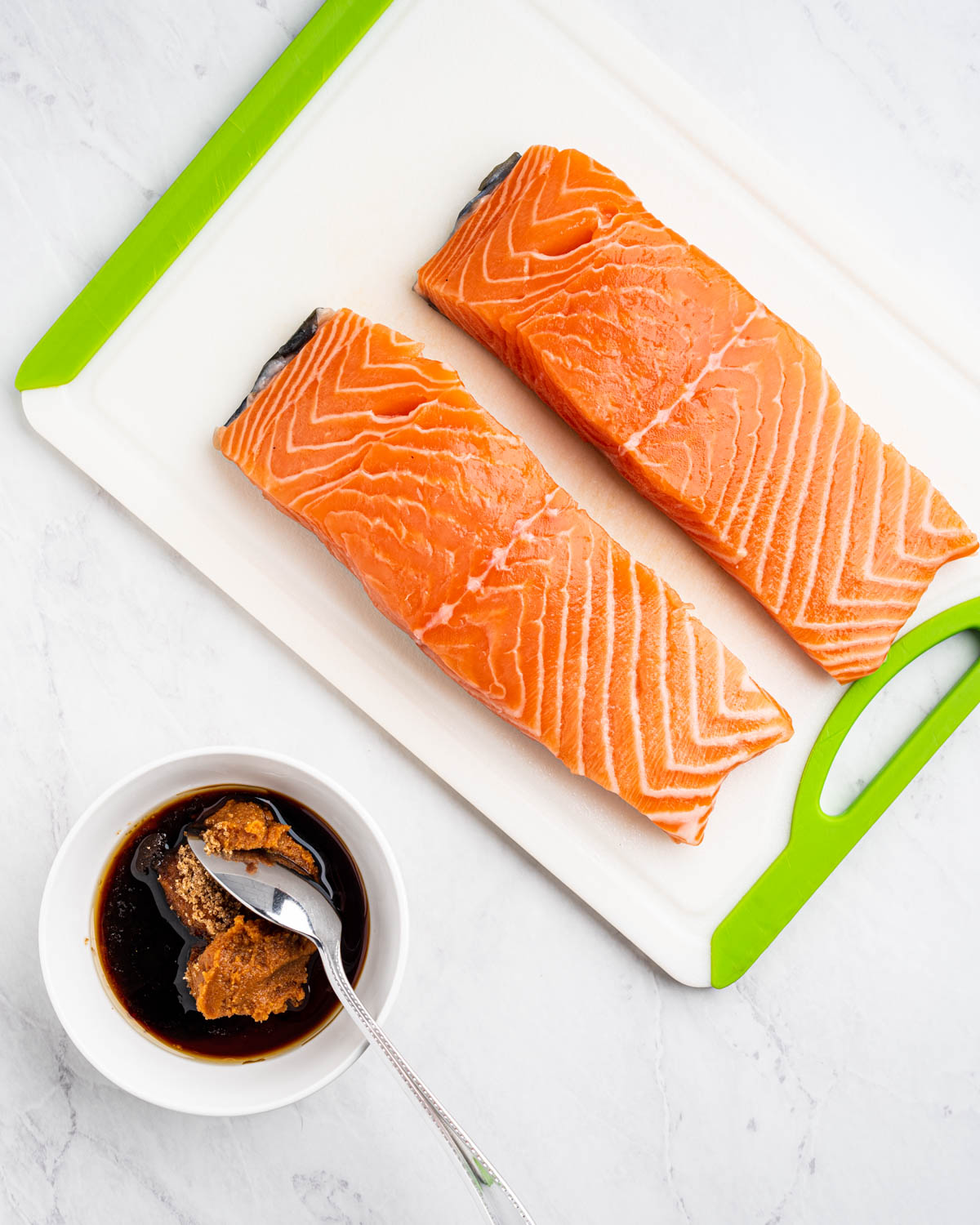 Two slices of salmon with miso glaze ingredients in a bowl.