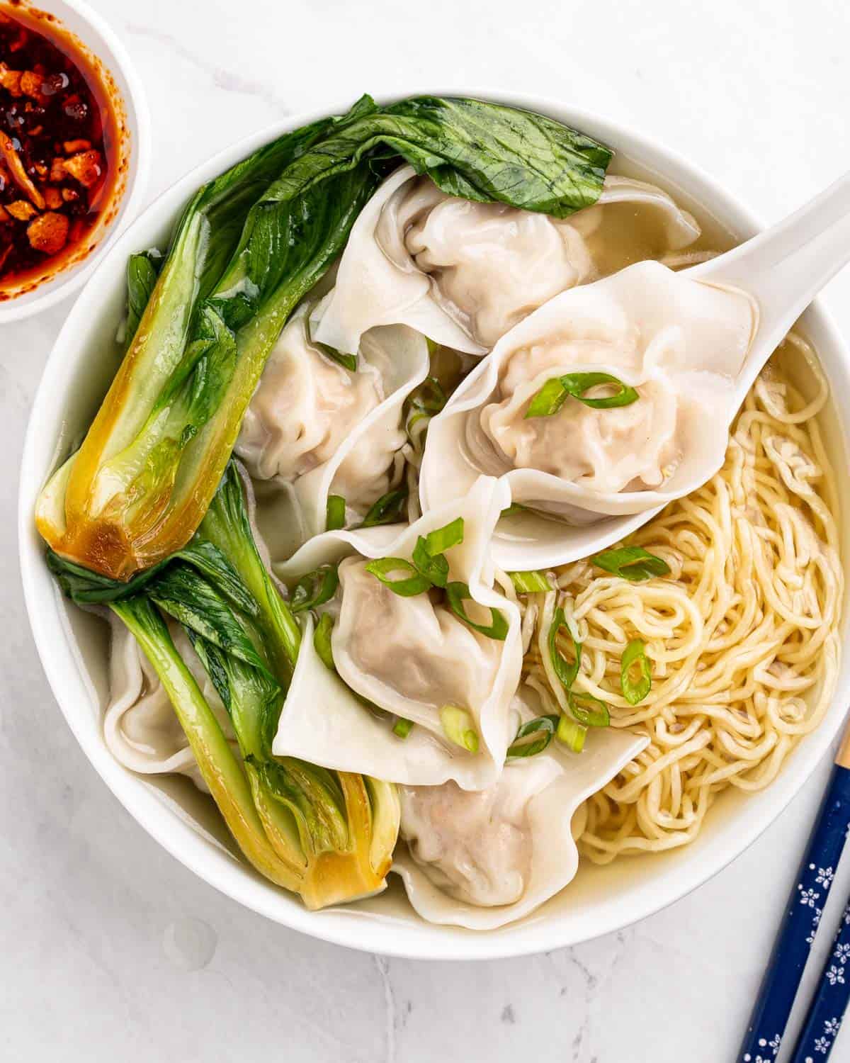 bowl of wonton soup with baby bok choy and side of chili oil.
