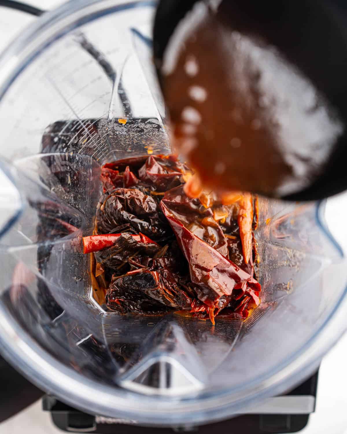 Cooked chili peppers in a blender with ladle adding broth.