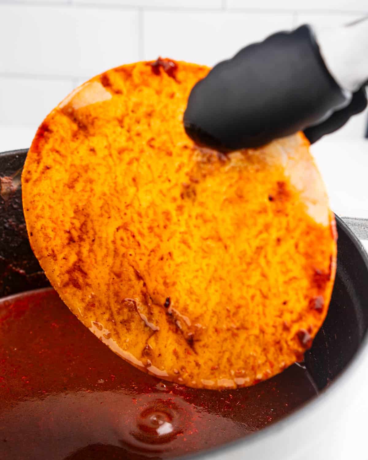 Tongs dipping corn tortilla into pot of consommé sauce.