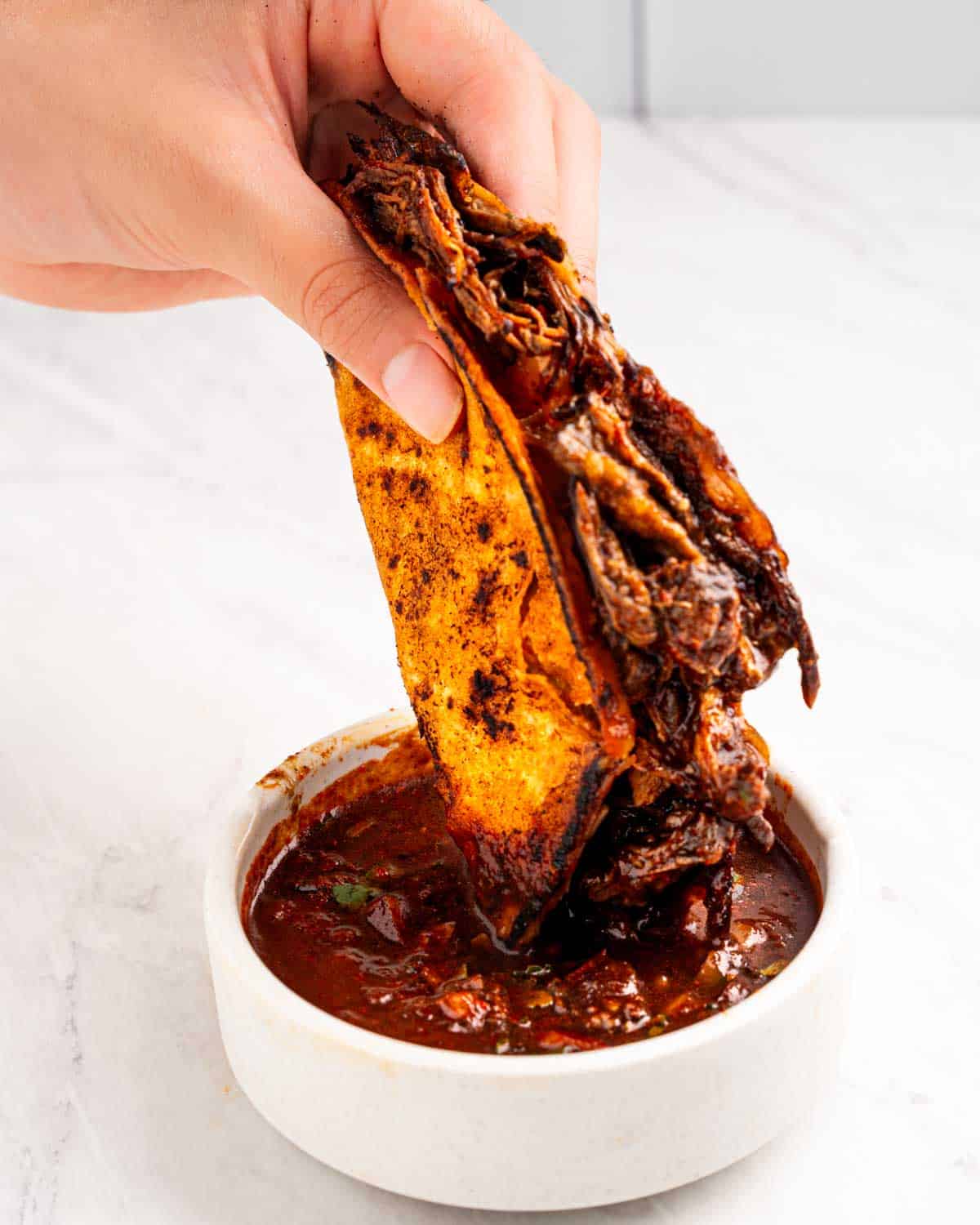 hand dipping birria taco into consommé sauce.