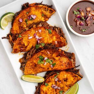 Birria Tacos on a plate with lime wedges and dipping sauce.