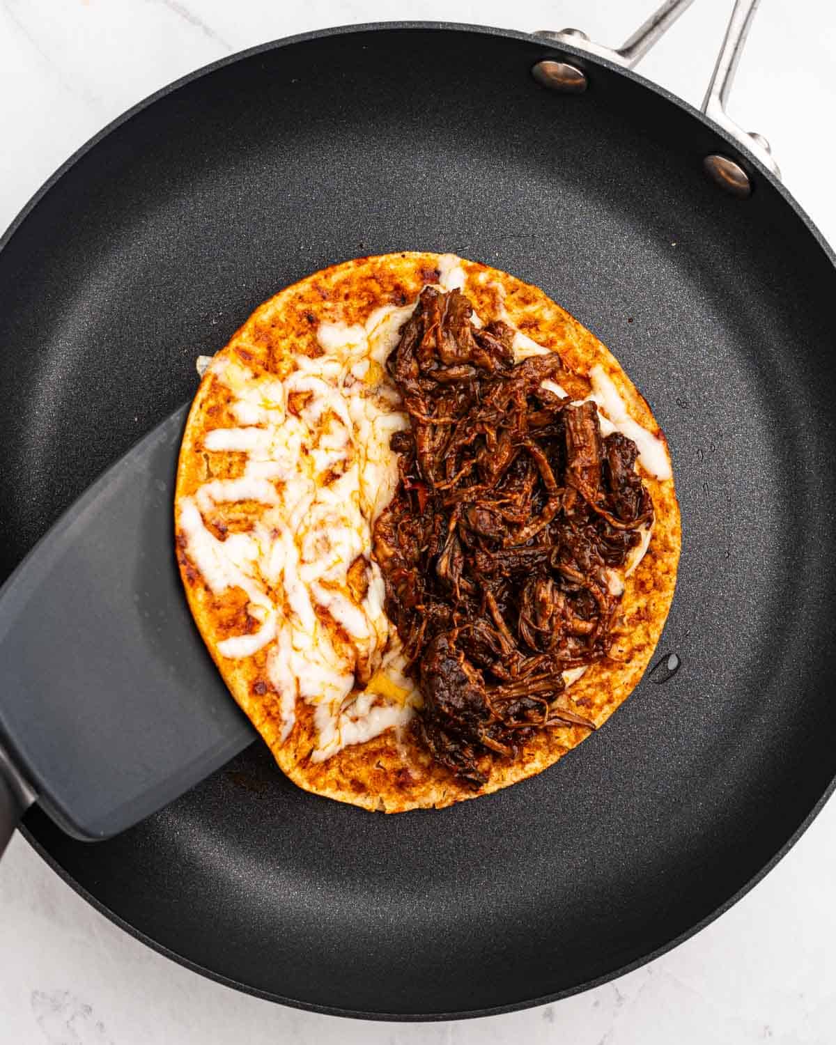 corn tortilla with melted cheese and birria meat on a pan.